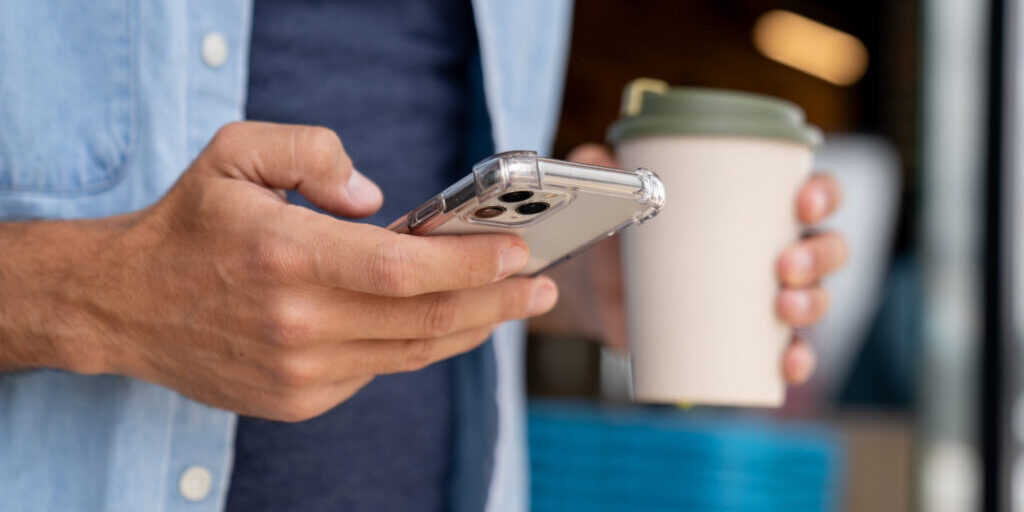 Close-up on a man using his phone and drinking coffee on the go