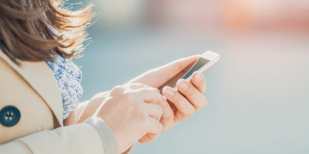 Young woman walking and using a smart phone on a city street.